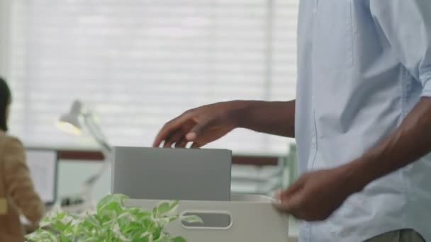 Afro-Amerikaanse zakenman inpakken van zijn bezittingen in doos tijdens de voorbereiding om kantoor te verlaten na ontslagen - Video