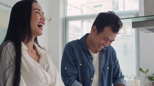 Tilt down shot of laughing Asian couple of man and woman cooking salad while preparing dinner at home - Footage, Video