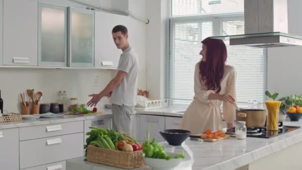 Średnie długoterminowe ujęcie pary młodych kaukaskich mężczyzn i kobiet gotujących razem obiad w kuchni - Materiał filmowy, wideo