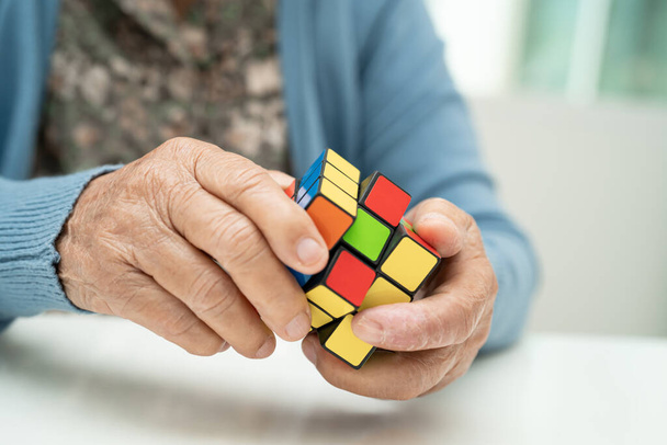 Бангкок, Таиланд 14 августа 2023 года Болезнь Альцгеймера AD, азиатская пожилая женщина, играющая в игру Rubik cube, чтобы практиковать тренировку мозга для предотвращения деменции. - Фото, изображение