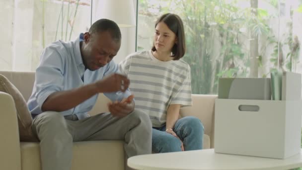 Amante esposa consolando seu marido afro-americano chateado sentindo-se estressado após a perda de emprego enquanto sentados juntos no sofá na sala de estar - Filmagem, Vídeo