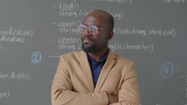 Portrait en gros plan d'un enseignant afro-américain debout devant un tableau noir regardant la caméra et souriant dans une salle de classe de programmation pendant la journée - Séquence, vidéo