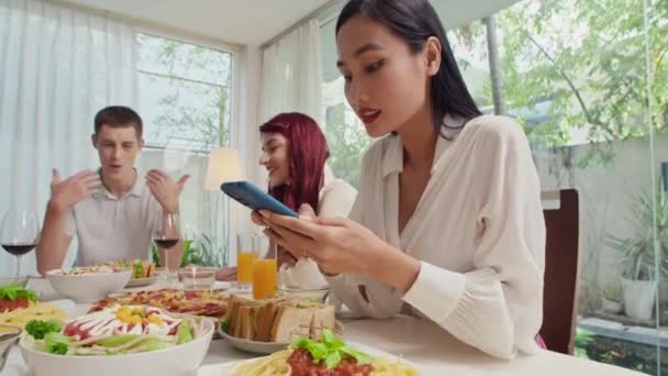 Mujer joven fotografiando platos caseros en la mesa festiva en el teléfono inteligente y mostrando fotos a su amigo, celebrando en casa - Metraje, vídeo