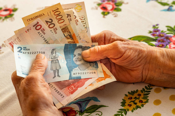 Колумбійське песо, пенсіонерка тримає в руці кілька банкнот, фінансові проблеми літніх людей, інфляція та бідність в Колумбії - Фото, зображення
