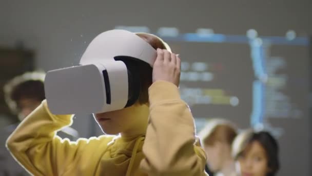 Close-up van de blanke basisleeftijd jongen zet VR bril op en rond te kijken in het klaslokaal, front licht aan de achterkant - Video