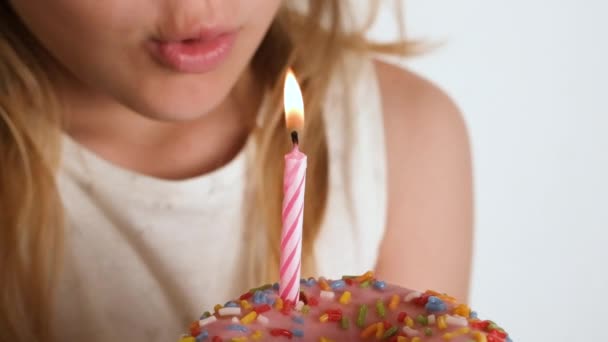 ピンクのドーナツにろうそくを吹き飛ばした少女. 誕生日や記念日のコンセプト。 願いのスローモーションフルHD誕生日ビデオを作る. - 映像、動画