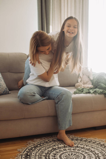 Madre piggybacks su pequeña linda hija sentada en el sofá disfrutar divertido tiempo de juego activo juntos en casa. - Foto, imagen
