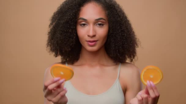 Piękno Afroamerykanka dziewczyna trzymać dwa pół pomarańczowe plastry pokrywają oczy dieta wegetariańska waga ciała ekologiczna zdrowa witamina skóra włosy pielęgnacja loki szampon owoce naturalne organiczne wegańskie cytrusy kosmetyczne - Materiał filmowy, wideo