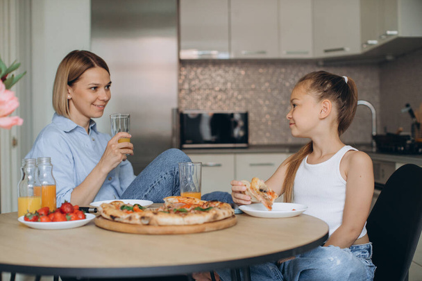 estilo de vida foto de la madre y la pequeña hija sonriendo y comiendo deliciosa comida juntos desayunando en casa por la mañana. - Foto, imagen