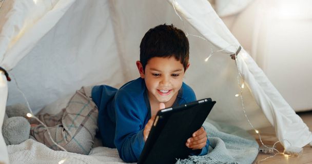 Tablette, se détendre et garçon enfant dans une tente jouer à un jeu en ligne sur Internet dans le salon. Heureux, divertissant et enfant regardant un film, une vidéo ou un spectacle sur une technologie numérique dans un fort de couverture. - Photo, image
