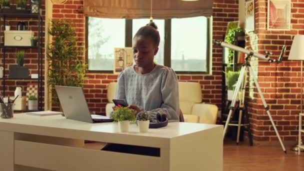 Vrouw freelancer navigeren webpagina en het controleren van social media app voor het oplossen van dagelijkse taken, netwerkverbinding. Afro-Amerikaanse zelfstandige telewerker zit aan bureau bij zonsondergang. - Video
