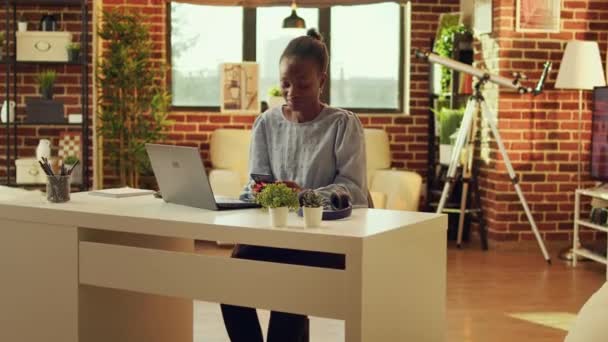 Kadın tele-işçi, günlük serbest işlere ve ağ bağlantılarına başlamadan önce web sayfasını karıştırıyor ve sosyal medyayı kontrol ediyor. Günbatımında masasında oturan Afrikalı Amerikalı serbest çalışan kişi.. - Video, Çekim