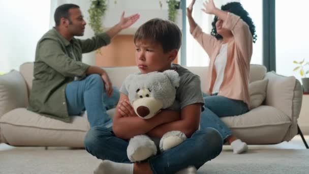 Overstuur blanke kleine jongen kleuterschool zoon knuffel teddy speelgoed terwijl Afro-Amerikaanse vrouw moeder en man vader in woede schreeuwen argumenteren achtergrond verdrietig kind lijden aan familieruzie conflict kind trauma - Video