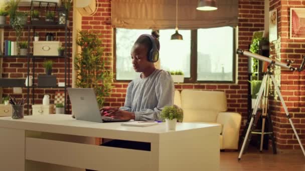 Freelancer lubi pracować na stacji roboczej słuchając muzyki i wykonując czynności internetowe. O zachodzie słońca, Afroamerykanka jest wielozadaniowa, kariera online w blogu. - Materiał filmowy, wideo