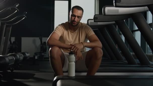 Únava Afroameričan atlet pitná voda bílkoviny doplňky ze sportovní láhve unavený sportovec běžec odpočinek tělo rekreace po kardio běh na běžícím pásu pocit žízně dehydratace nápoj - Záběry, video