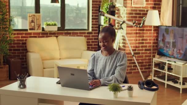Thuis gebaseerde Afrikaanse Amerikaanse ontwikkelaar begint dag door het oplossen van opdrachten voor online netwerken baan. Vrouw freelancer met behulp van laptop op werkstation om te reageren op e-mails, natuurlijk licht bij zonsondergang. - Video