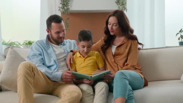 Happy caucasian family dad mom son reading fairytale story book on sofa in cozy living room caring loving mother father teaching child kid boy schoolboy read learning education enjoying hobby at home - Footage, Video
