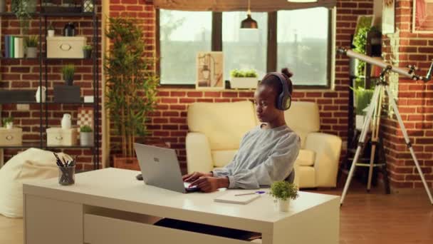 Gelukkige werknemer luistert naar muziek, typt informatie op laptop thuis. Afro-Amerikaanse freelancer het creëren van online carrière, genieten van externe baan tijdens het zingen van liedjes vanaf de hoofdtelefoon. - Video