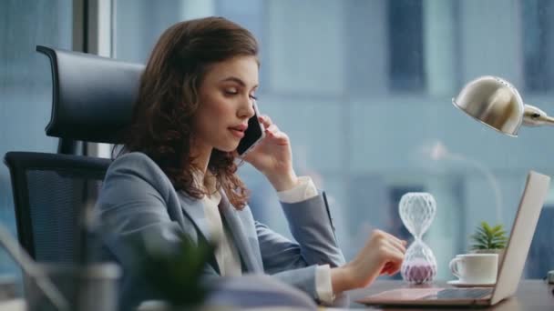Kiireinen nainen soittaa työpöydän ääreen läheltä katsottuna. Vakava houkutteleva liikenainen puhuu älypuhelin yrityksen työpaikalla. Nuori nainen pomo keskustella työstä puhelimessa. - Materiaali, video