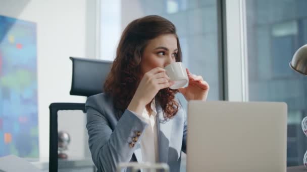 Бізнес-леді насолоджуються перервою на каву, сидячи на сучасному офісному столі крупним планом. Спокійна розслаблена жінка-менеджер, яка п'є напої на робочому місці компанії, дивлячись ноутбук. Приваблива леді працівник працює за комп'ютером. - Кадри, відео