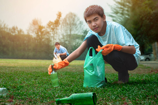 Asiatische Jungen sammeln ausrangierte Glas- und Plastikflaschen auf einem Hof der Gemeinde in Plastiktüten, um sie zu recyceln oder zu verkaufen, um Geld für sein tägliches Leben zu verdienen.. - Foto, Bild