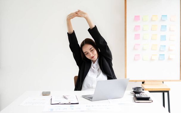 Asiática contable mujer está cansada de trabajar en una silla, estiramiento para relajarse y relajarse mientras trabaja duro en la oficina. - Foto, Imagen