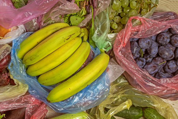 banane verdi si trovano in cima ad altre verdure e frutta in sacchetti di plastica multicolore. flatlay - Foto, immagini