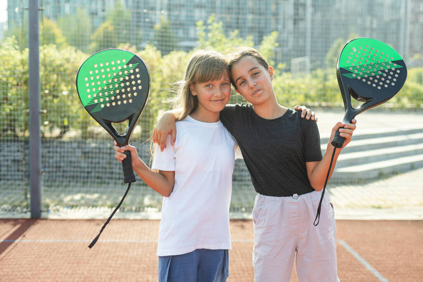 Девочки-подростки с ракетками и мячами стоят на площадке, смотрят в камеру и улыбаются. Высокое качество фото - Фото, изображение