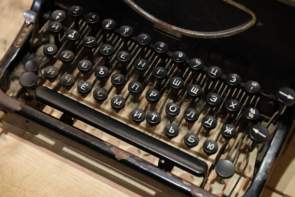 Détails d'une vieille machine à écrire rétro de style vintage avec des surfaces poussiéreuses sur une table en bois à l'intérieur sombre - Photo, image