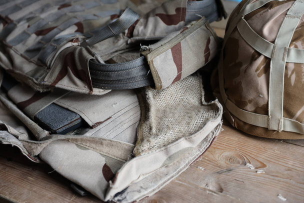 Um capacete militar de um soldado ucraniano com um colete à prova de balas pesado na mesa de madeira no interior do checkpoint dugout - Foto, Imagem