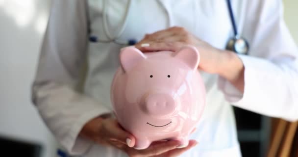 Nurse doctor woman with stethoscope holding pink piggy bank. Health insurance health care and medicine - Footage, Video