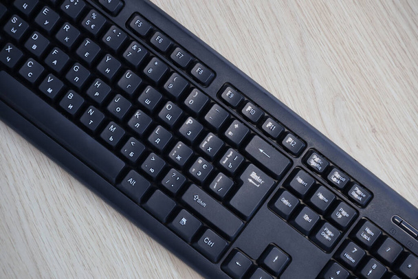 Маленькая компактная черная игровая клавиатура на столе из деревянных сосновых досок. Беспроводная клавиатура с механическими выключателями для гаджетов и компьютера. Копирование пространства - Фото, изображение