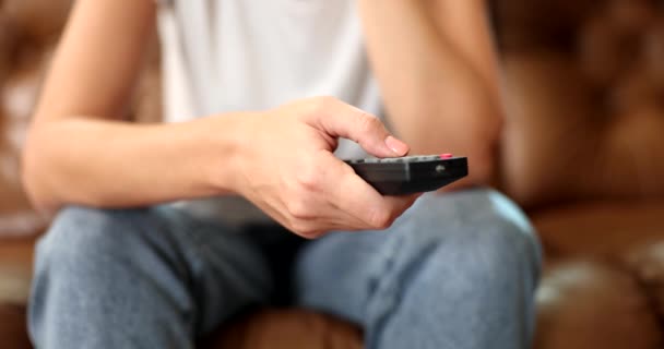 Vrouwelijke hand met TV afstandsbediening drukknop terwijl u op de bank zit. TV aanzetten en kanaal selecteren - Video