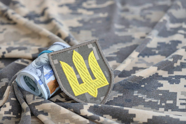 Simbolo dell'esercito ucraino e banconote da un mucchio di dollari sull'uniforme militare. Pagamenti ai soldati dell'esercito ucraino dagli Stati Uniti, stipendi ai militari. Sostegno alla guerra in Ucraina - Foto, immagini