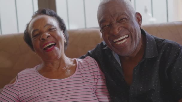 Felice coppia anziana ridendo e sorridendo seduto sul divano guardando la fotocamera. Gioioso pensionato brasiliano volti primi piani, autentica vita reale ridere e sorridere trasudante felicità - Filmati, video