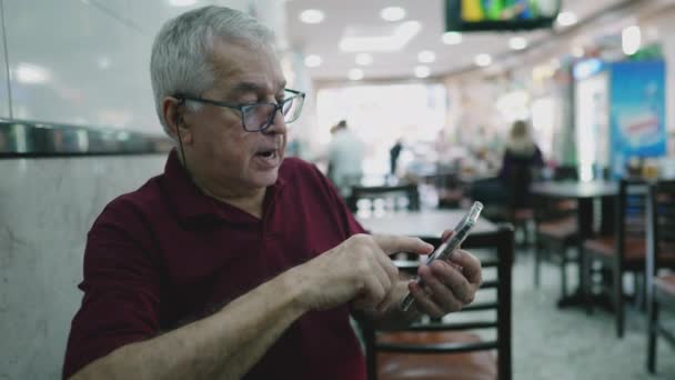 Senior man met behulp van mobiele telefoon apparaat gezeten in restaurant business - Video