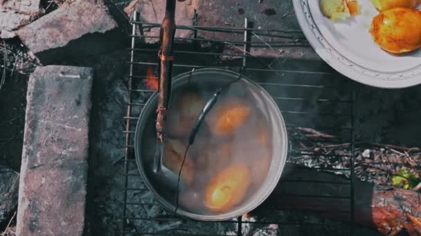 Patatesler gün boyunca açık bir ateşin üzerinde büyük bir kazanda pişirilir. Ormanda piknik. Tencere yanıyor ve su kaynıyor. Bir kamp tenceresi odun ateşinde yeni patatesler pişirir.. - Video, Çekim