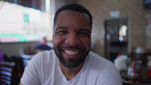 Een vrolijke zwarte Braziliaanse man glimlachend naar de camera in het traditionele cafetaria restaurant. Close-up gezicht van een vrolijk portret - Video