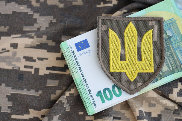 Ukraiński symbol armii i kilka banknotów euro na mundurze wojskowym. Wypłata żołnierz ukraiński armia z europejski unia, pensja wojskowy. Wsparcie wojenne dla Ukrainy - Zdjęcie, obraz