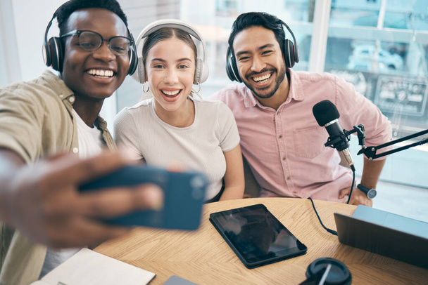 Podcast, uśmiech i grupowe selfie przyjaciół łączące, streaming na żywo i osoby nagrywające transmisję w studio. Szczęśliwy zespół hostów radiowych zrobić zdjęcie przy stole dla mediów społecznościowych lub współpracy. - Zdjęcie, obraz