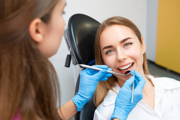 Een vrouwelijke patiënt met een vlekkeloze glimlach krijgt tandheelkundige zorg van de tandarts - Foto, afbeelding