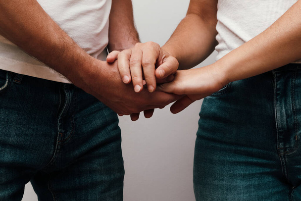Gesneden foto van een onherkenbaar koppel in jeans dragen elkaars hand vast, close-up. Close-up van een Kaukasisch koppel dat elkaars hand vasthoudt. Liefde en zorg concept. - Foto, afbeelding