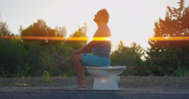 Ο άνθρωπος κάθεται στην τουαλέτα στο φόντο του ηλιοβασιλέματος. Υψηλής ποιότητας 4k πλάνα - Πλάνα, βίντεο