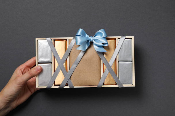 Шоколад в коробке с лентой в руке на сером фоне, вид сверху - Фото, изображение