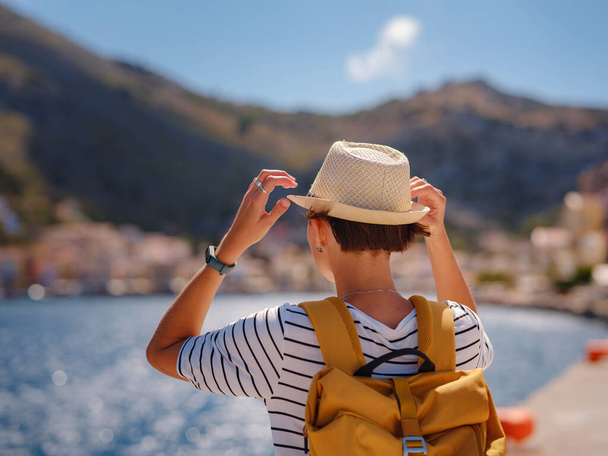 Schöne asiatische Happy Female mit Rucksack, die ihren Urlaub auf Symi Islands genießt. Blick auf den Hafen Symi oder Simi, winzige Insel Dodekanes, Griechenland, ruhige Atmosphäre und fabelhafte Architektur. - Foto, Bild