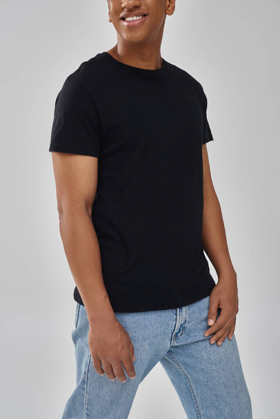 modelo masculino afroamericano elegante posando en camiseta negra y pantalones vaqueros, espacio de copia para la publicidad - Foto, Imagen
