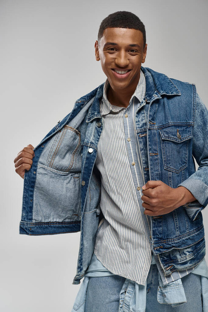 handsome emotional african american man in denim outfit posing on white backdrop, fashion concept - Photo, Image