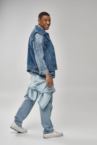pohledný emoční africký Američan v džínovém kostýmu pózující na bílém pozadí, módní koncept - Fotografie, Obrázek