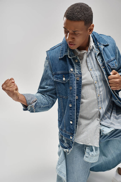 handsome emotional african american man in denim outfit posing on white backdrop, fashion concept - 写真・画像