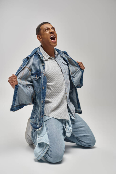 όμορφος συναισθηματικός Αφροαμερικάνος με denim στολή ποζάρει σε λευκό φόντο, fashion concept - Φωτογραφία, εικόνα